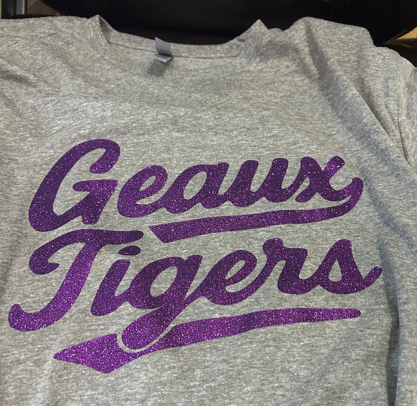 Gray shirt with purple 'Geaux Tigers' text on a person wearing a black jacket.